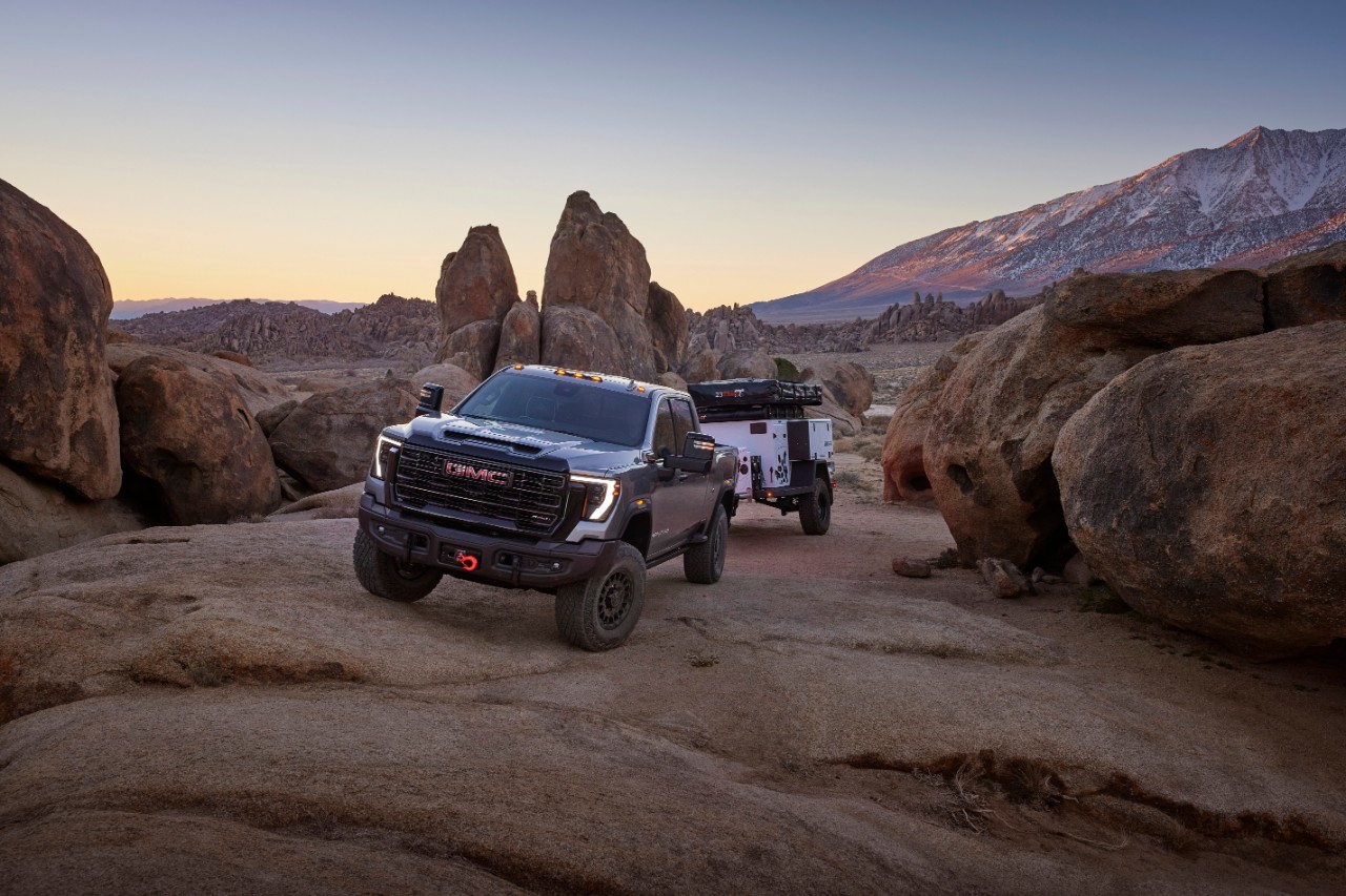 2024 GMC Sierra 2500HD AT4X AEV Edition towing an off-road trailer through rugged terrain.