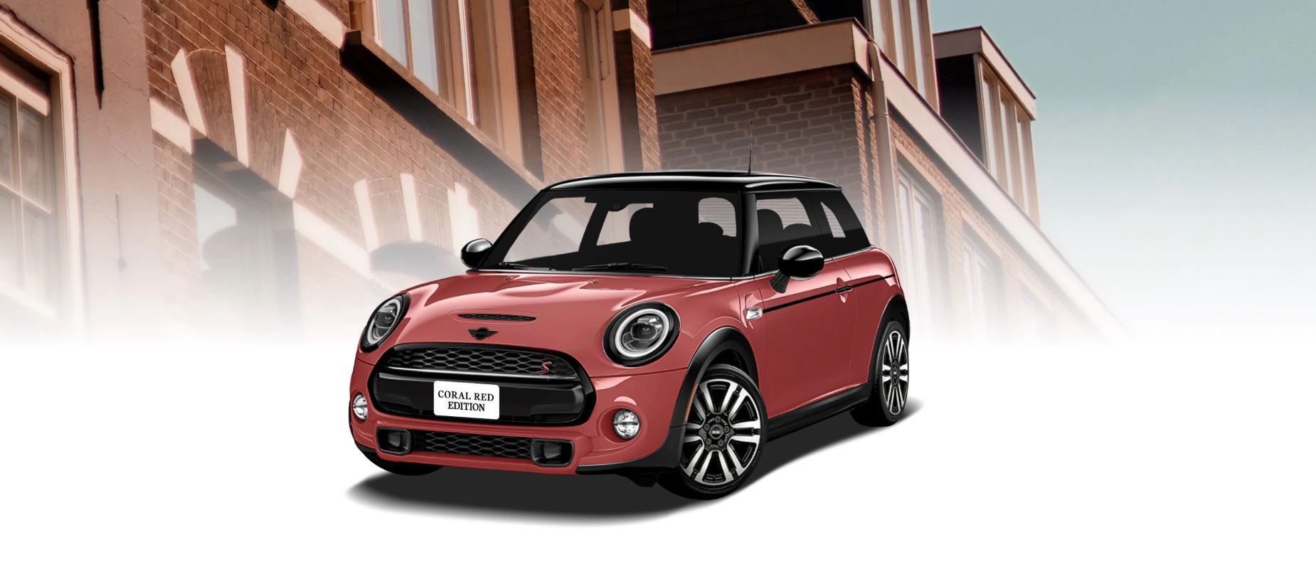 The MINI COOPER HARDTOP CORAL RED EDITION in front of a brick building.