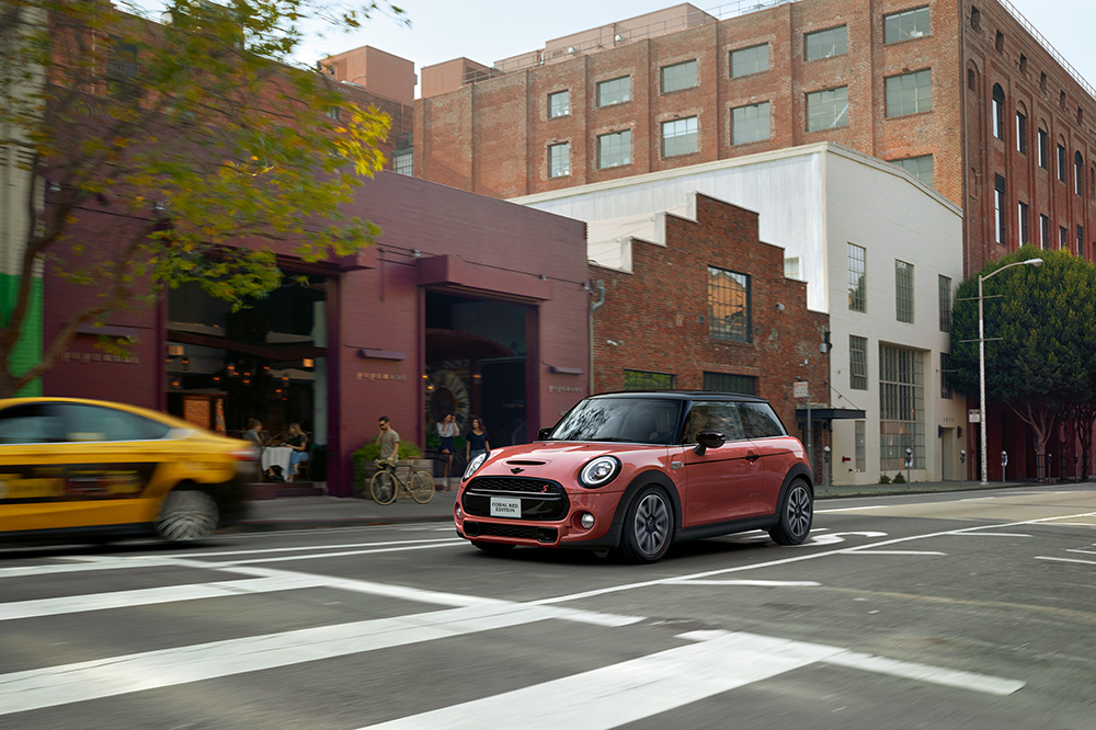 The MINI COOPER HARDTOP CORAL RED EDITION driving in the city.