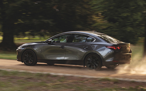 A gray Mazda3 driving on a dusty road