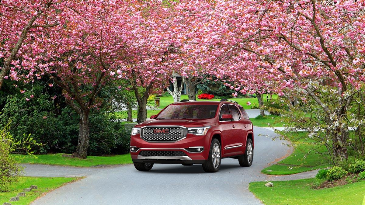 A red 2018 GMC Acadia leaving a blooming driveway.