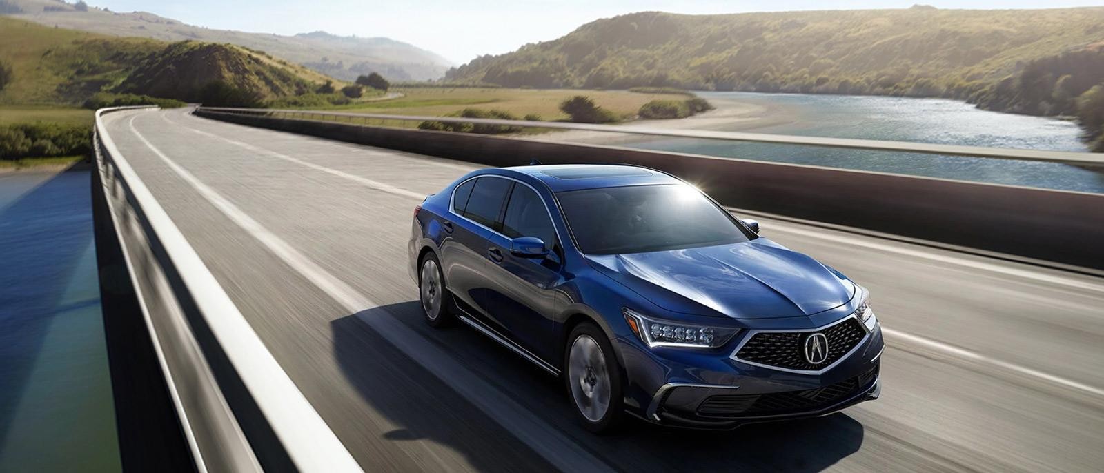 A blue Acura RLX driving across a bridge in the countryside.