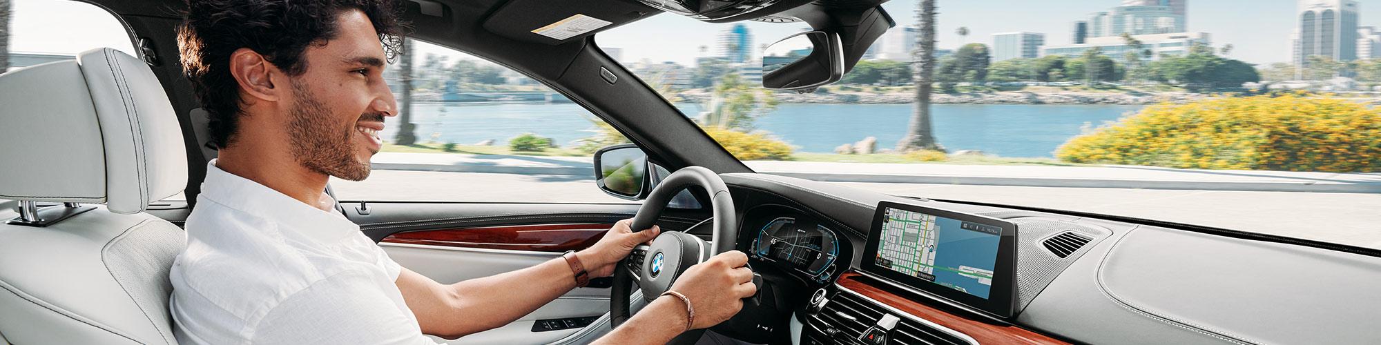 A happy man driving his BMW 5-Series along a city's waterfront.