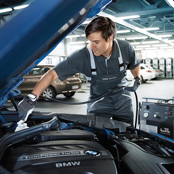 A BMW certified service technician topping off a vehicle's fluid levels.