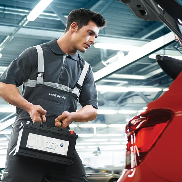 A BMW certified service technician installing a new battery in a vehicle.