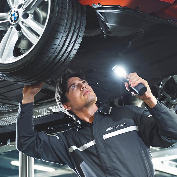 A BMW certified service technician inspecting under a vehicle.