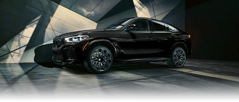 A black BMW X6 M parked in a modern courtyard.
