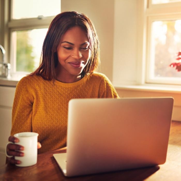 A woman holding a coffee mug and working on a computer.