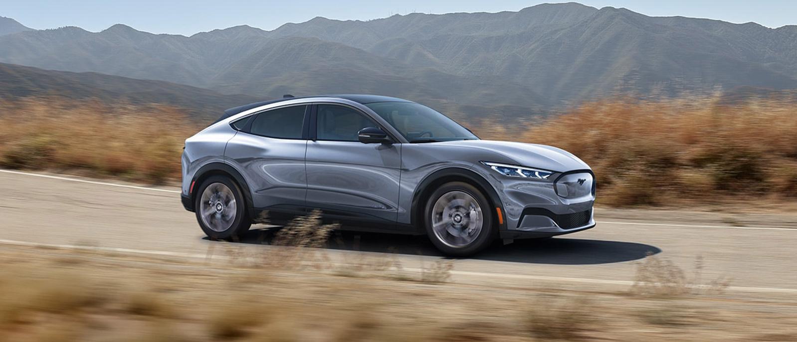 A Silver 2022 Ford Mustang Mach-E is sprinting on the road. A Silver 2022 Ford Mustang Mach-E is sprinting on the road.