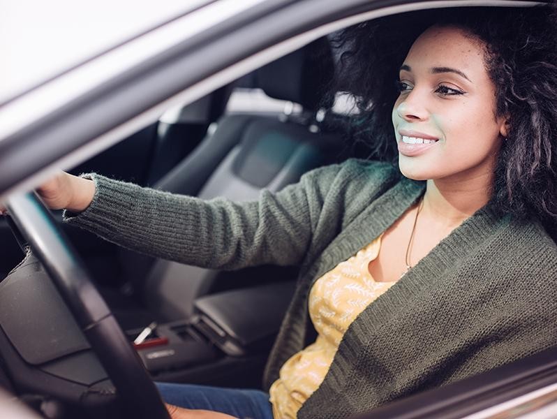 A smiling young woman in the driver's seat of a car.