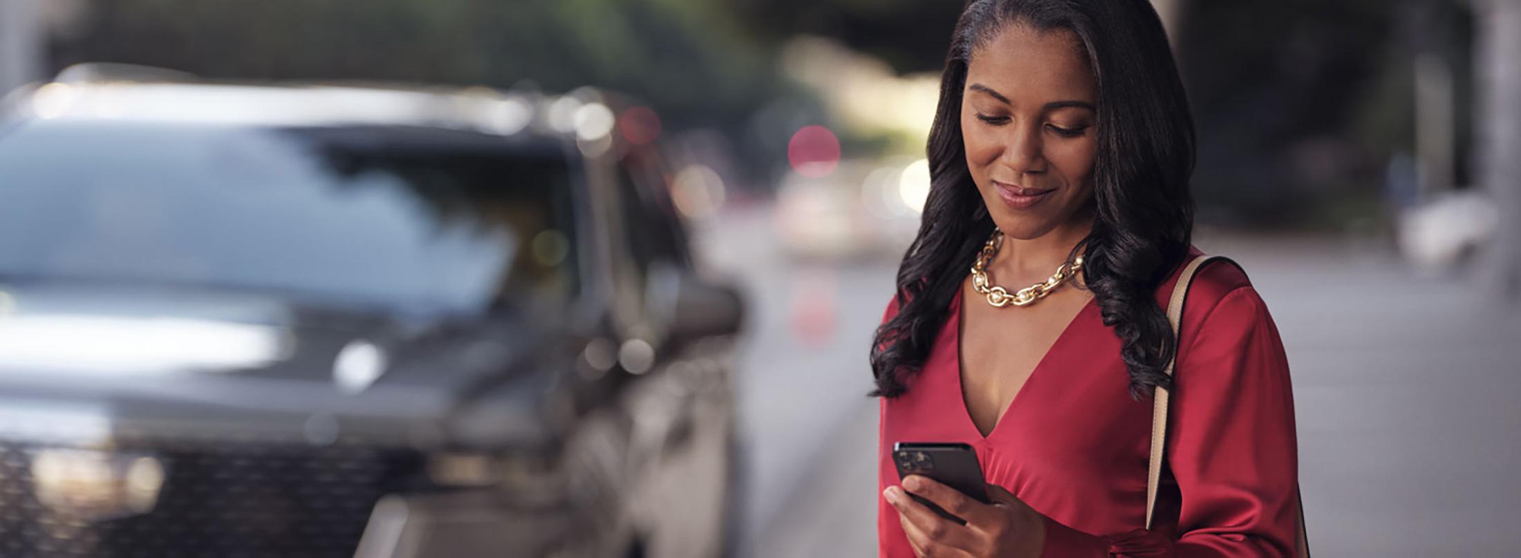 Black woman looking at cell phone in red dress with Cadillac blurred in background