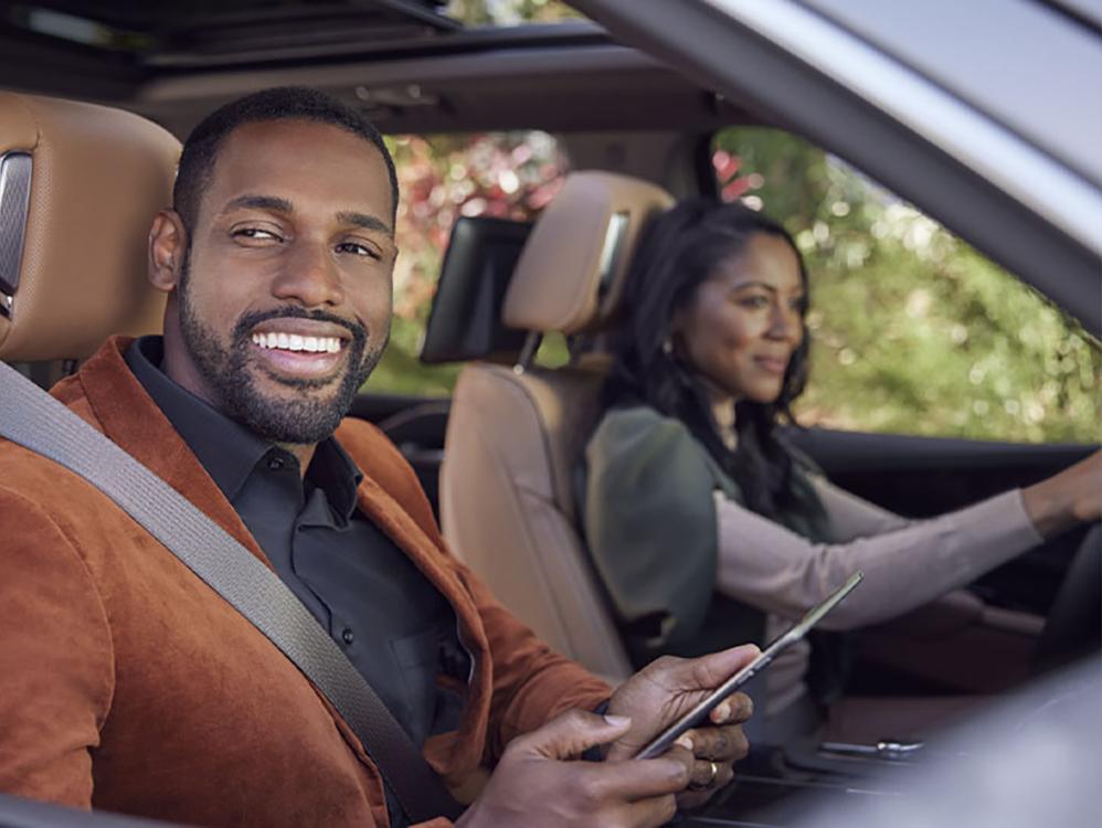 Black man inside cadillac holding an ipad smiling with black woman in drivers seat
