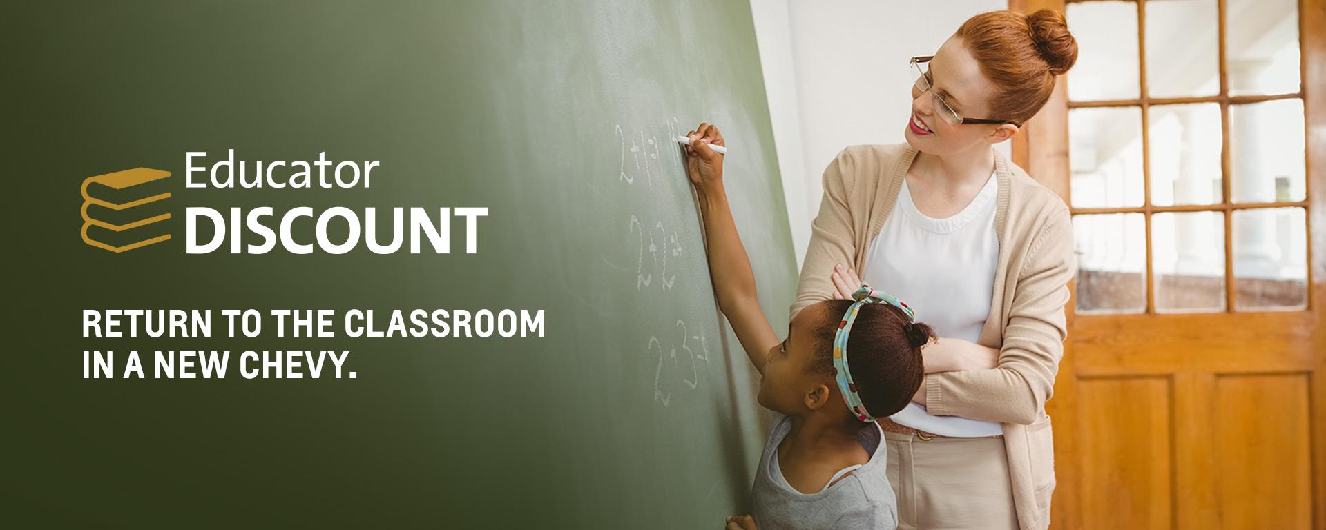 Woman teacher watching a small girl writing on a chalkboard