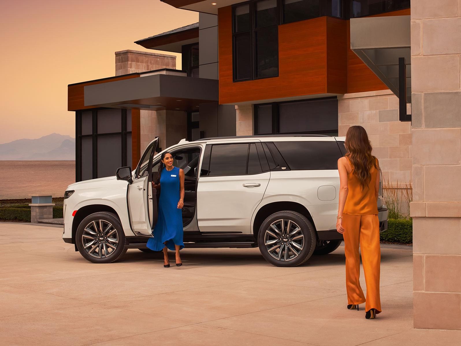 A Cadillac representative delivering a white Escalade to a woman at her desert home.