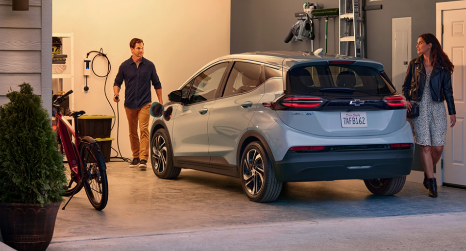A Couple In Their Garage With the Man Plugging in the Charger for Their Chevrolet Bolt EV