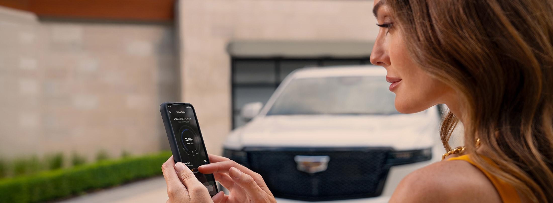 2022 Certified Service; Cadillac Certified Service; CS; Escalade Phone App; Woman holding phone with Escalade and building in background.