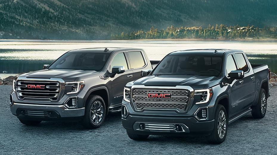 A lineup of GMC Sierra 1500 trucks parked in front of a mountain lake.