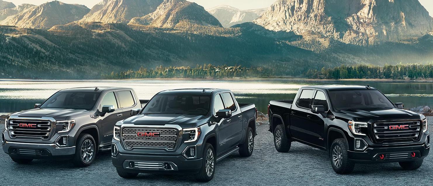 A lineup of GMC Sierra 1500 trucks parked in front of a mountain lake.