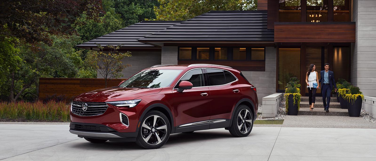 A red Buick Envision parked in the driveway of a modern home with a couple approaching. A red Buick Envision parked in the driveway of a modern home with a couple approaching.
