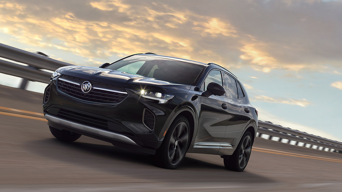 A Buick Envision driving along a curved road at sunset.