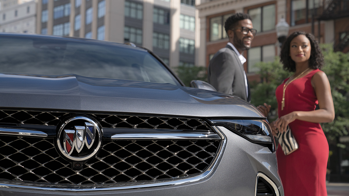 Front view of a Buick Envision's grille with a couple standing in the background.