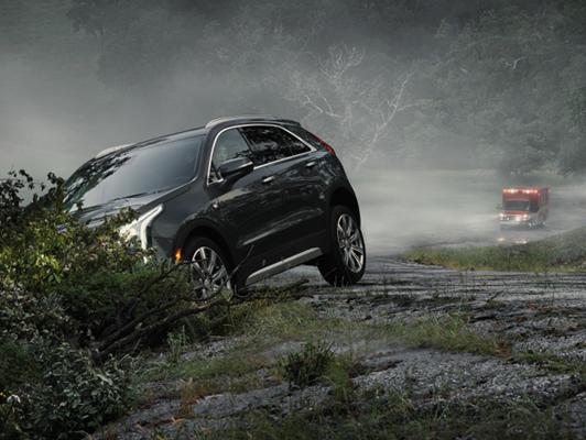 Cadillac vehicle in ditch with emergency vehicle behind it