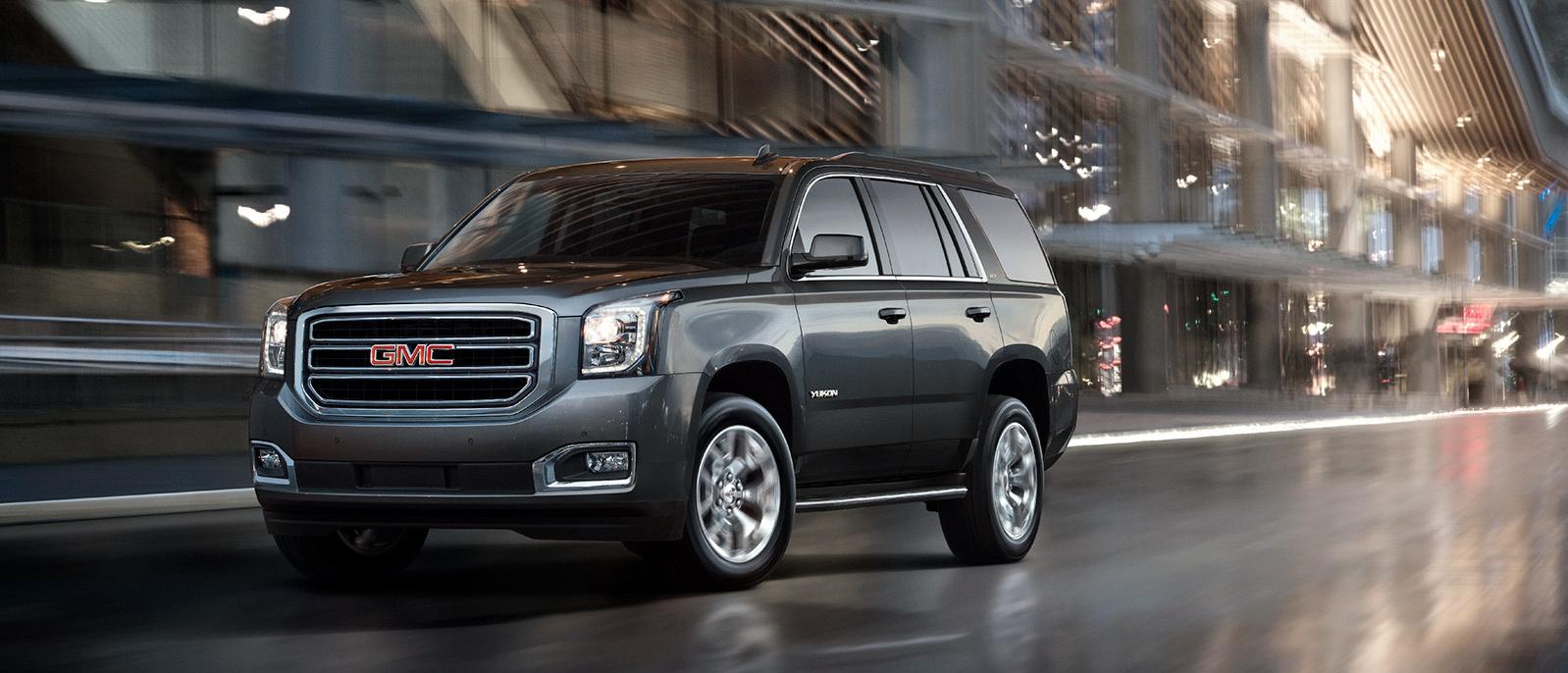 A silver 2020 GMC Yukon driving through a city street. A silver 2020 GMC Yukon driving through a city street.