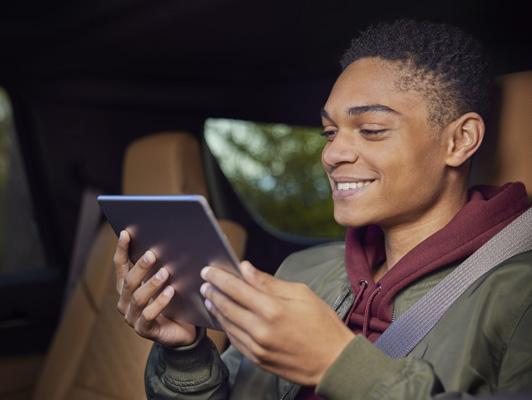 Young black man in back seat of cadillac with tablet smiling Young black man in back seat of cadillac with tablet smiling