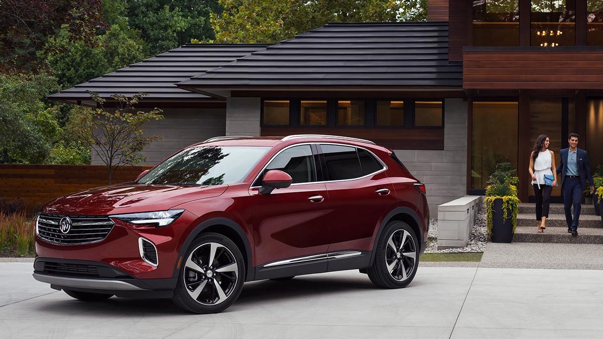 A red Buick Envision parked in the driveway of a modern home with a couple approaching.