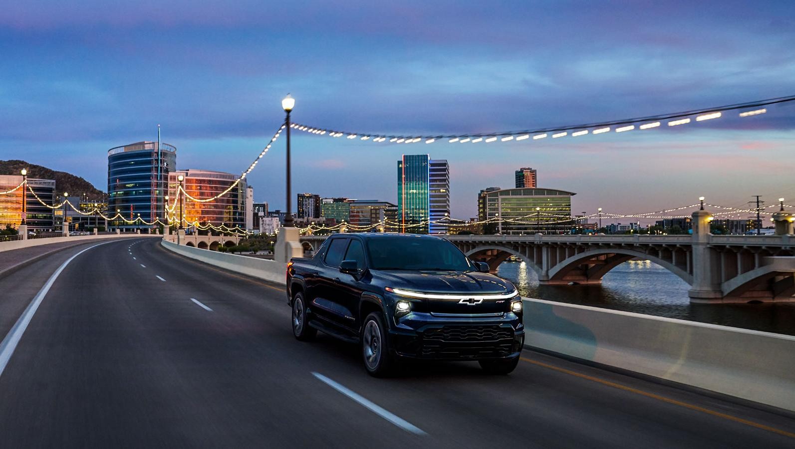 Black 2024 Chevrolet Silverado EV driving in a city near water