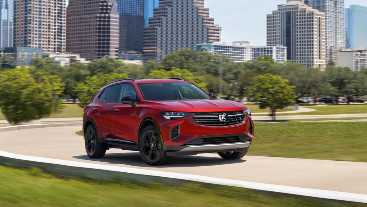 2023 Buick Envision on road with city, grass and trees in background.