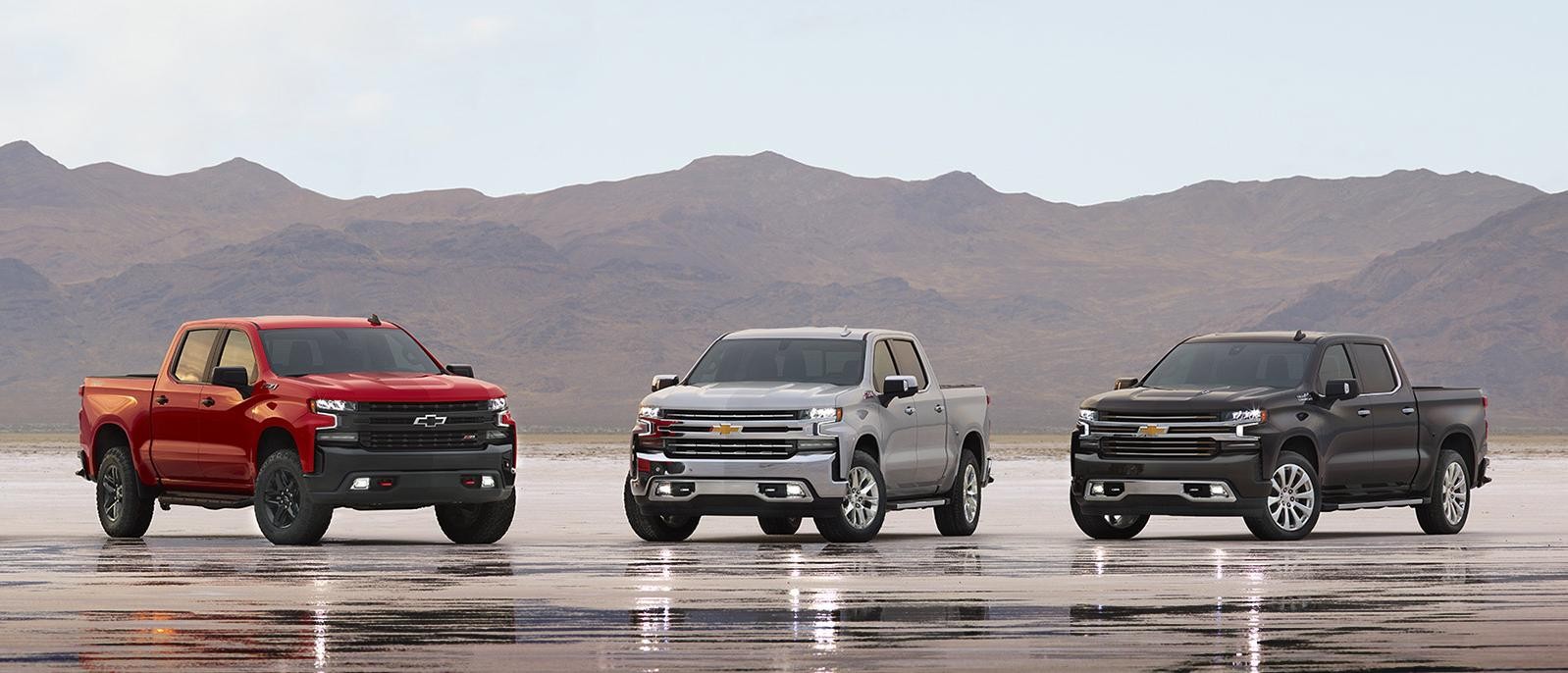 Three Silverado 1500 models on a wet salt-flat in the desert at dusk.