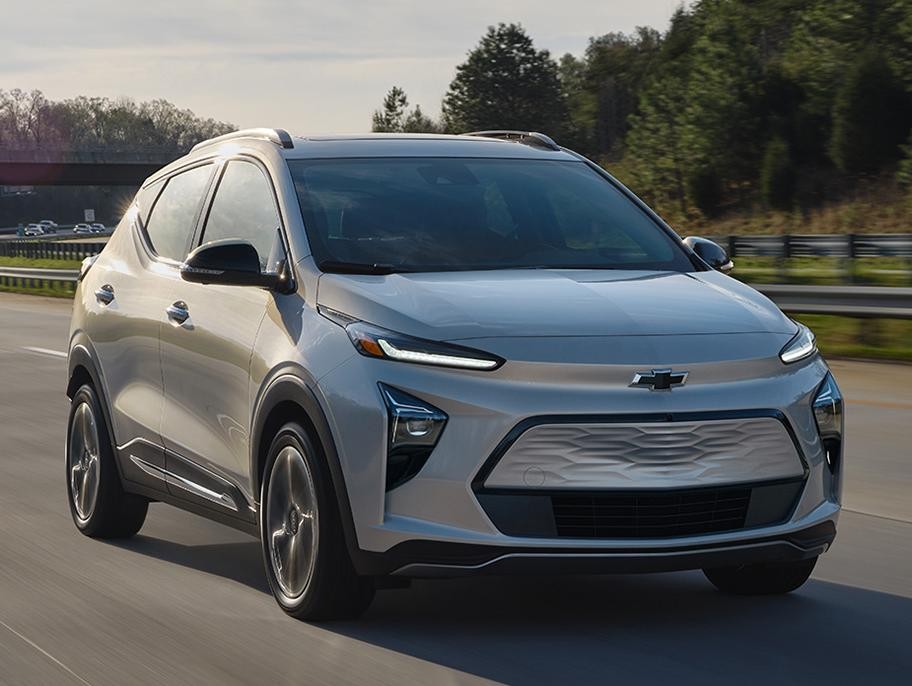 A light blue Chevy Bolt EUV driving on a countryside highway.