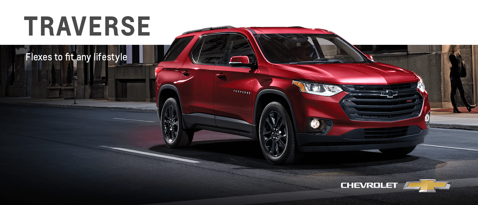 A red Chevy Traverse driving down a city street at night.