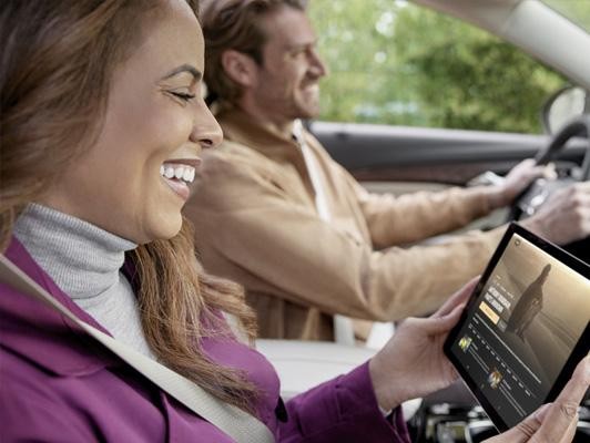 Woman in foreground with tablet watching movie with man driving in background