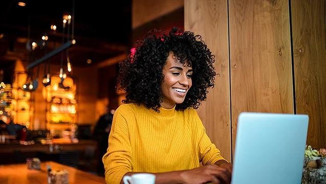 woman in yellow shirt on a laptop in a cafe