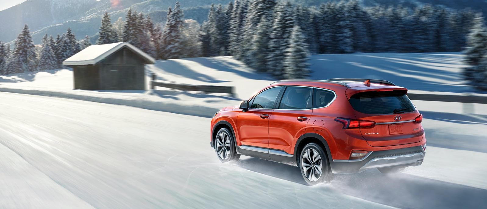 An orange Hyundai Santa Fe driving along a snowy country road.