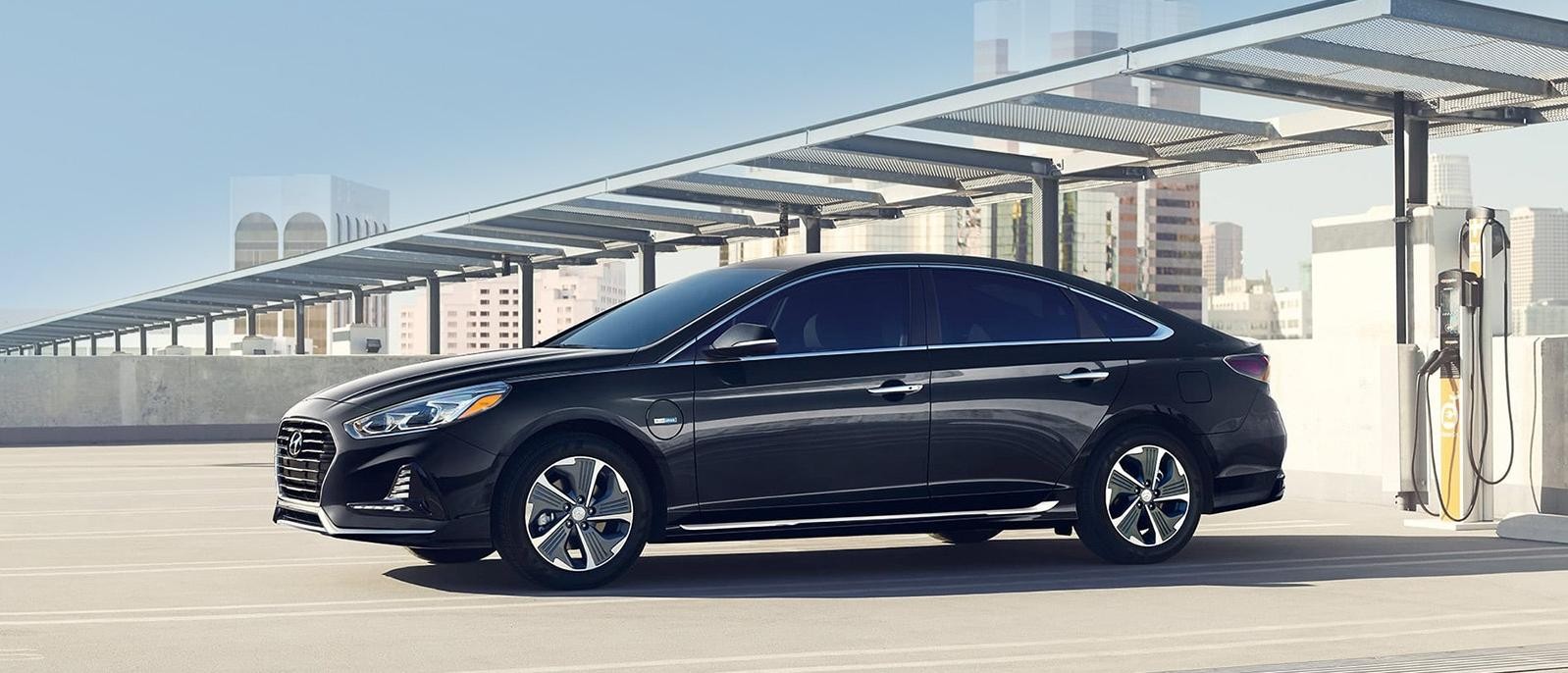 A grey Hyundai Sonata Plug-In Hybrid parked at a rooftop parking lot with charger stations.