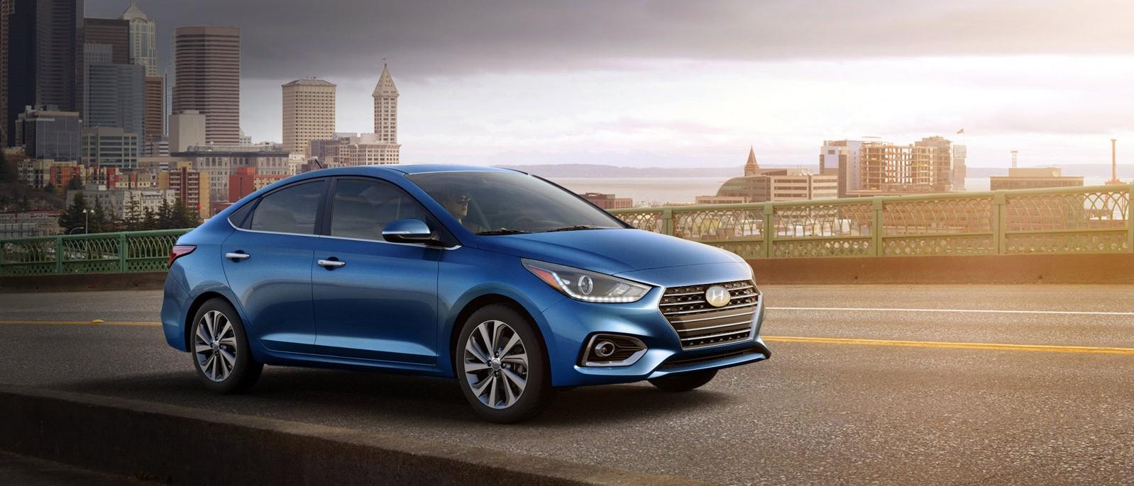 A blue Hyundai Accent driving away from a city.