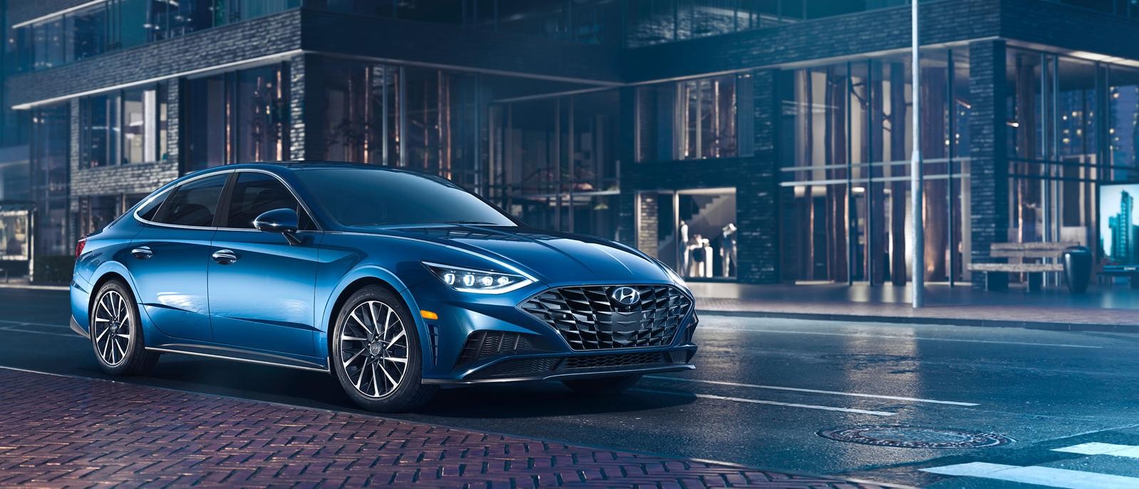 A blue Hyundai Sonata parked on a city street at night.