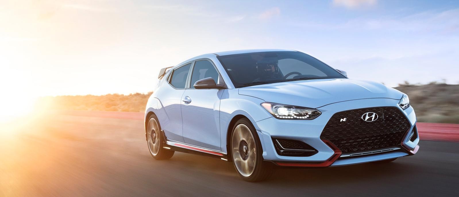 A white Hyundai Veloster driving on a desert highway at sunset.