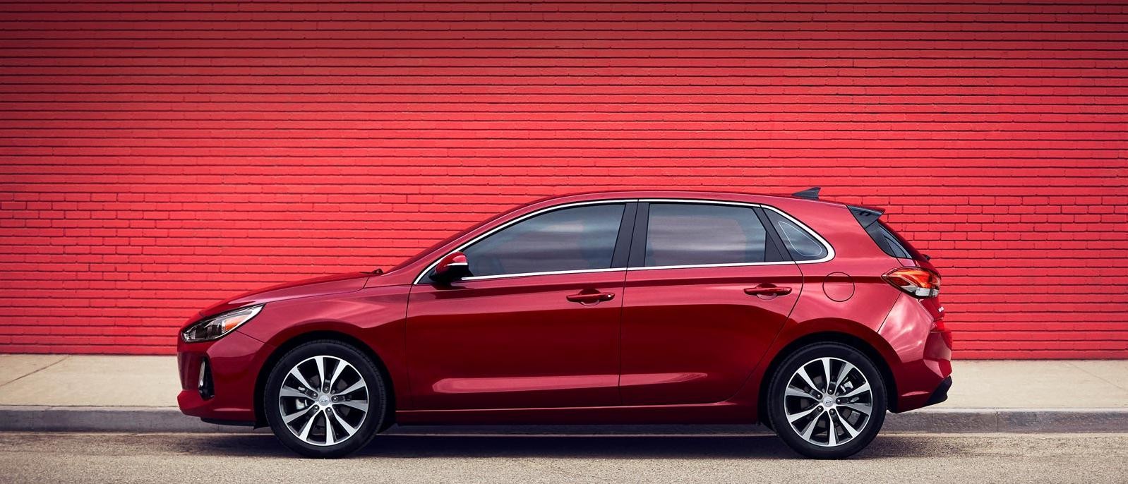 A red Hyundai Elantra GT parked in front of a red brick wall.