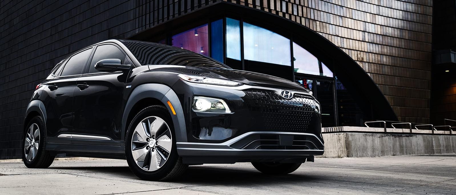 A Black Hyundai Kona EV parked in front of the arched entry of a downtown building.