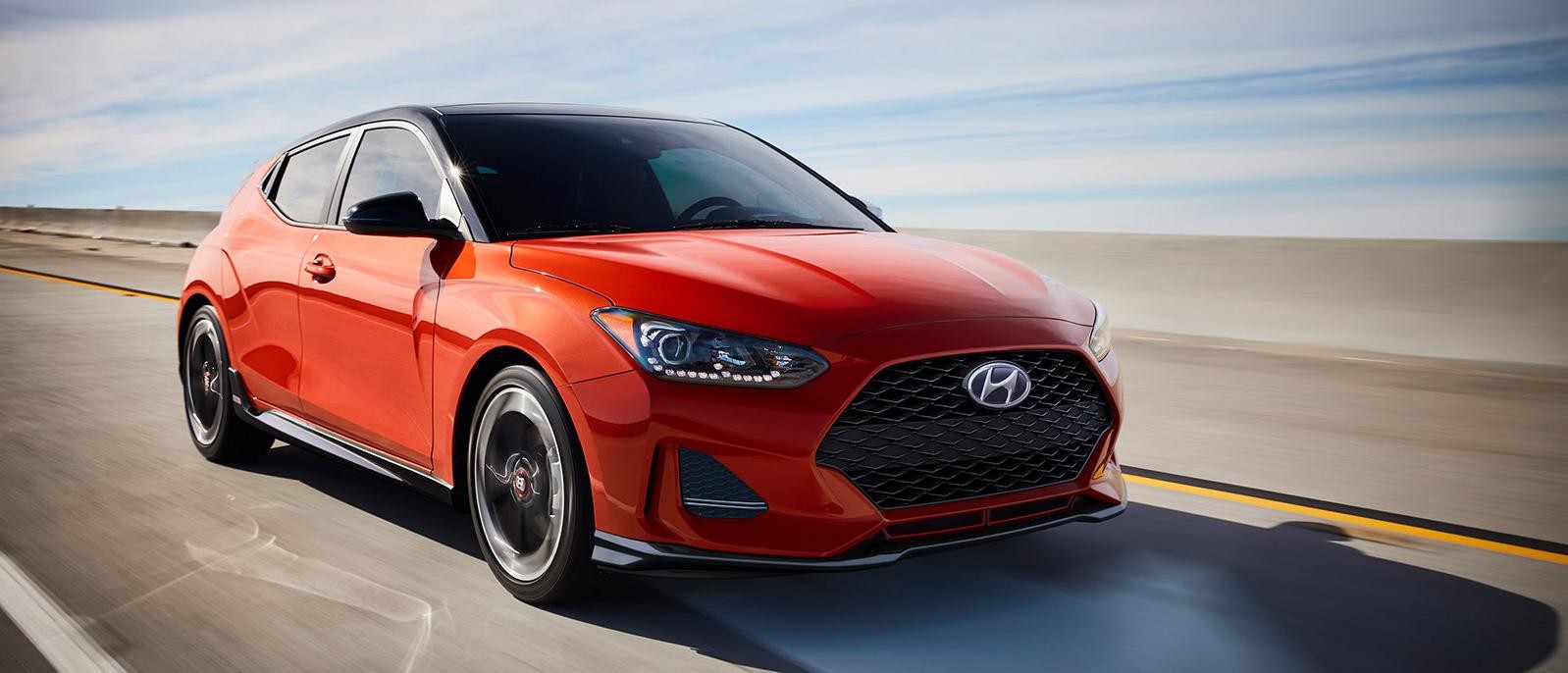 A orange Hyundai Veloster driving on a desert highway.
