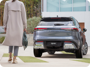 Rear view of a woman walking towards her Moonbow Blue INFINITI QX60 in the driveway.