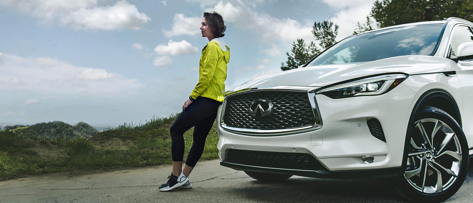 A woman leaning against her INFINITI QX50 on a country road. A woman leaning against her INFINITI QX50 on a country road.