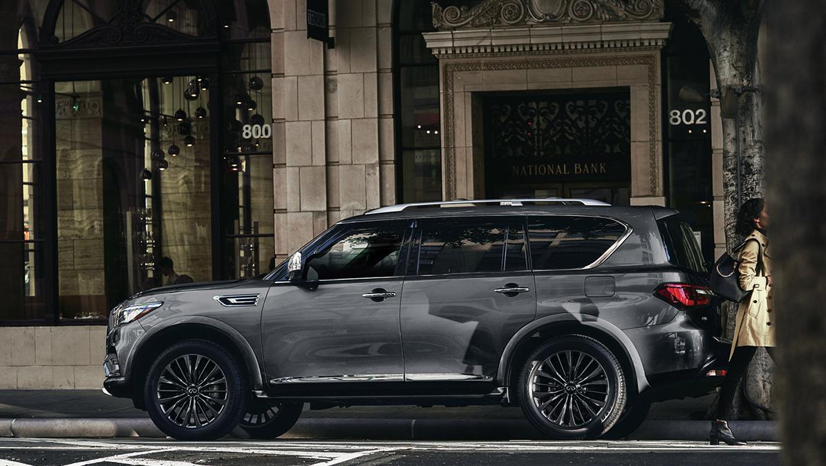 Profile view of a grey INFINITI QX80 parked in front of an old city bank. Profile view of a grey INFINITI QX80 parked in front of an old city bank.