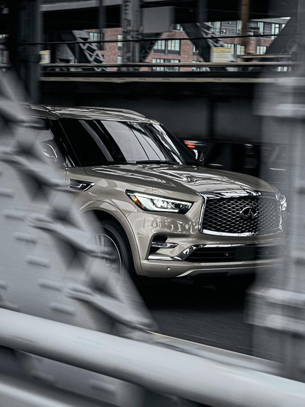 A peek-a-boo view of a grey INFINITI QX80 driving over a bridge. A peek-a-boo view of a grey INFINITI QX80 driving over a bridge.