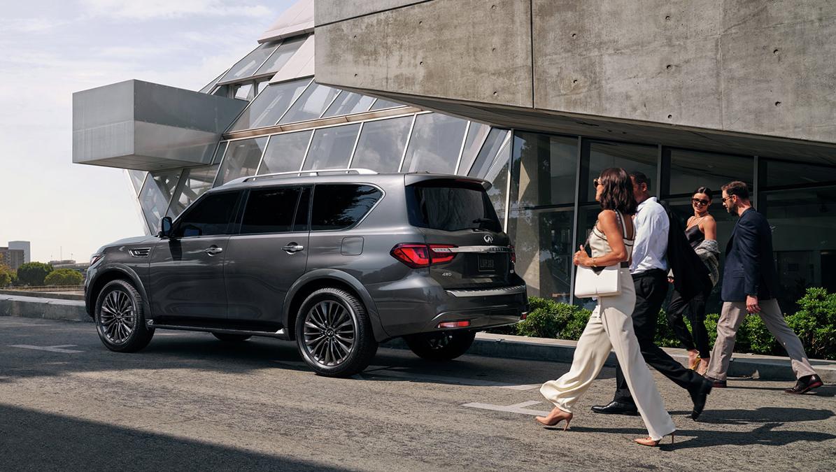 A grey INFINITI QX80 parked in front of a concert hall with people approaching. A grey INFINITI QX80 parked in front of a concert hall with people approaching.