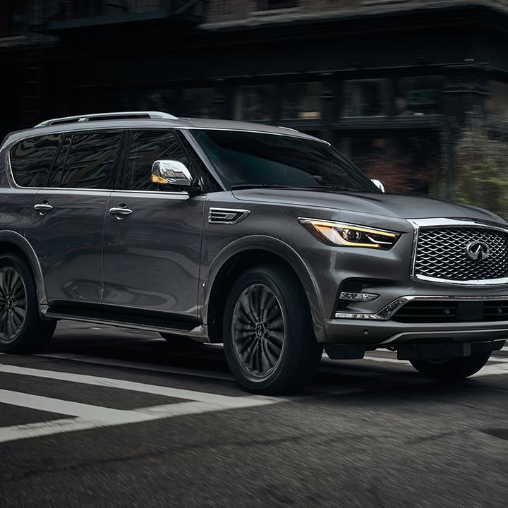 Side view of an INFINITI QX80 driving around a city corner. Side view of an INFINITI QX80 driving around a city corner.